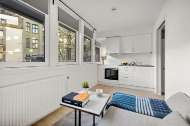 Jasny salon z aneksem kuchennym, sofą i stolikiem, z dużymi oknami.