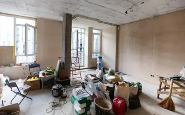 Niedokończone wnętrze mieszkania w remoncie, z drabiną i porozrzucanymi materiałami budowlanymi.