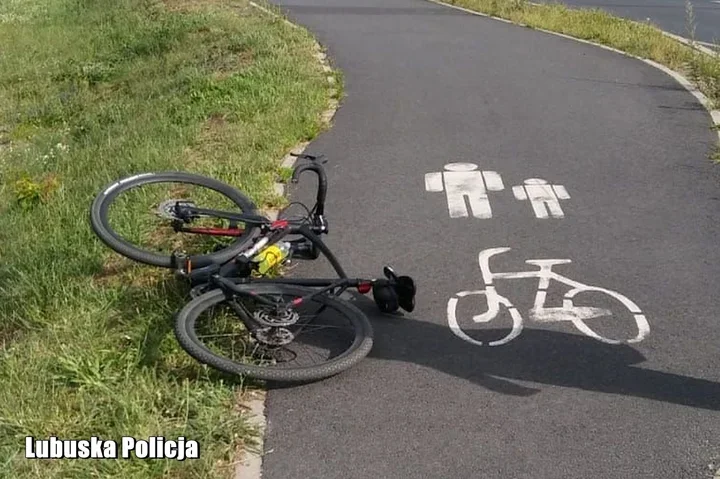 Rower leżący na poboczu ścieżki rowerowej oznaczonej symbolami pieszych i roweru.