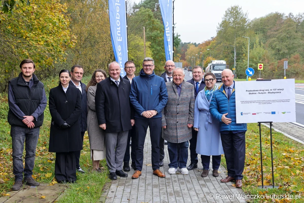 Grupa osób pozuje do zdjęcia podczas uroczystości otwarcia przebudowanej drogi wojewódzkiej nr 137 w jesiennej scenerii.