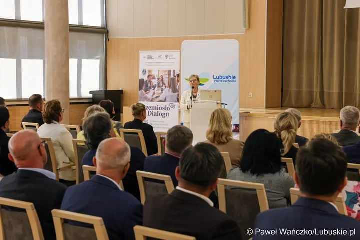 Kobieta w białym garniturze przemawia z mównicy do publiczności zgromadzonej w sali konferencyjnej, w tle banery z napisami „Lubuskie Warte zachodu” i „Rzemiosł