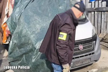 Funkcjonariusz oznaczony opaską „Policja” stoi przy białym furgonie Fiat na terenie zabudowanym, zdjęcie udostępnione przez Lubuską Policję.
