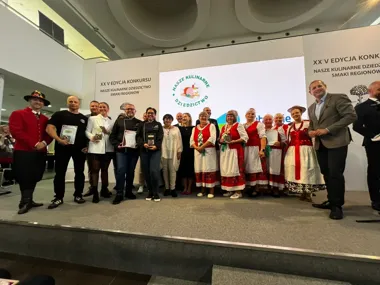 Grupa osób, w tym kucharze i kobiety w strojach ludowych, stoi na scenie podczas XX edycji konkursu "Nasze kulinarne dziedzictwo - smaki regionów".