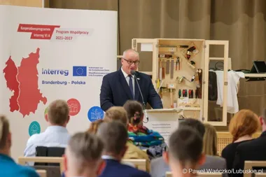 Mężczyzna w garniturze przemawia zza pulpitu do publiczności podczas wydarzenia promującego program Interreg Brandenburgia-Polska 2021-2027.