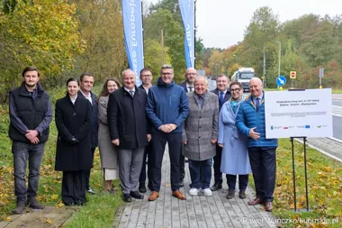 Grupa osób pozuje do zdjęcia podczas uroczystości otwarcia przebudowanej drogi wojewódzkiej nr 137 w jesiennej scenerii.
